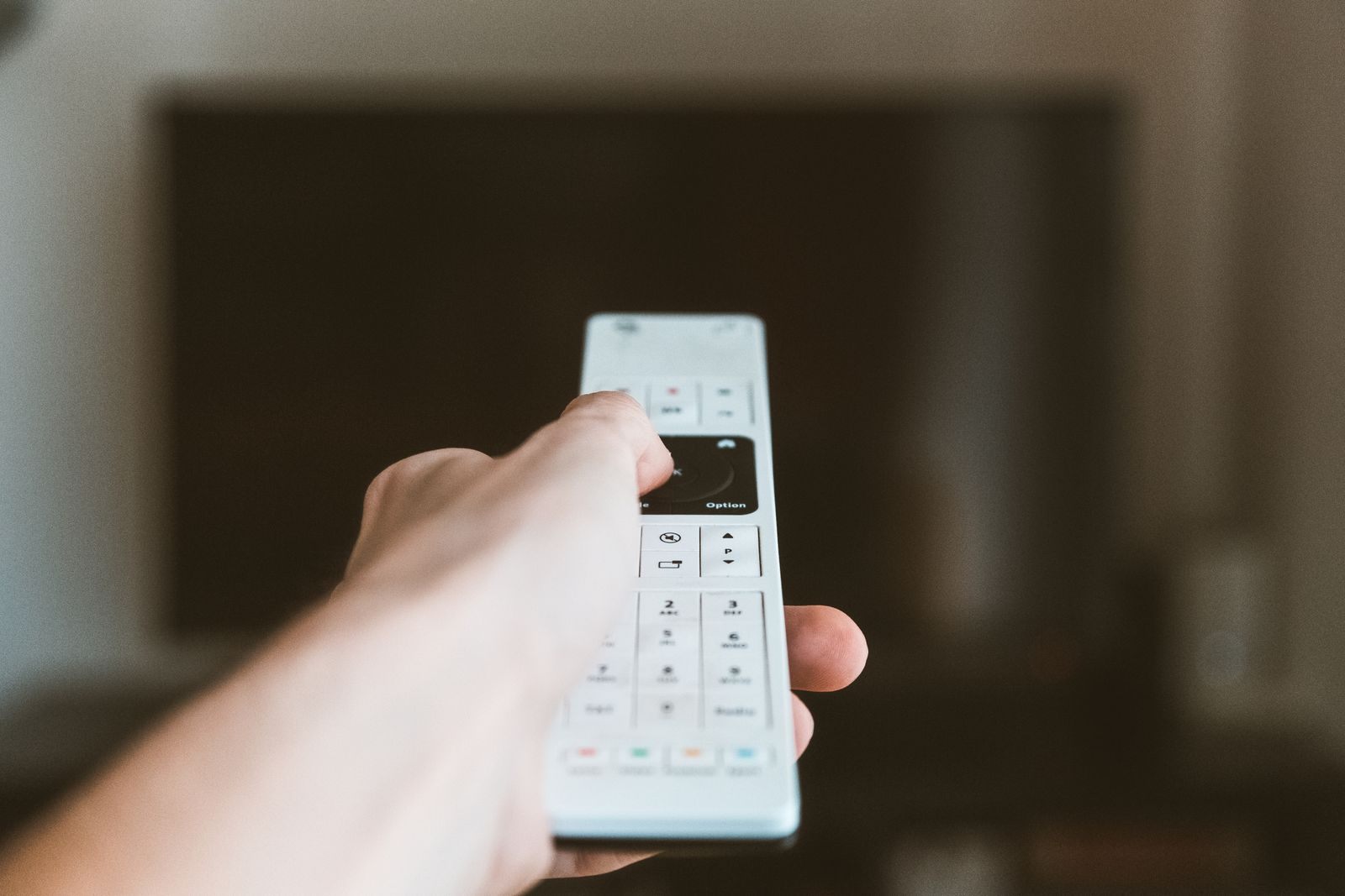 Hand pointing a remote at a television while cruise deals on TV play